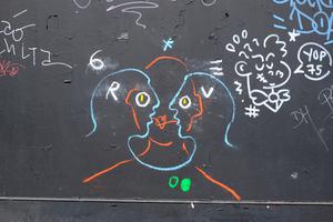 Tag sur un mur parisien. Trois silhouettes entremêlées.